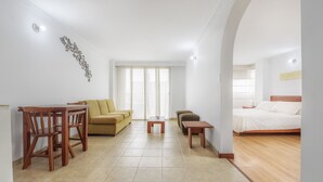 A hotel room with a bed, a sofa, a dining table with chairs, a small table, and a decorative wall piece. - Hotel Alicante (Bogotá)