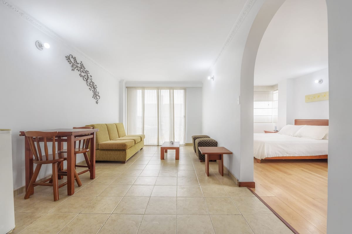 A hotel room with a bed, a sofa, a dining table with chairs, a small table, and a decorative wall piece.