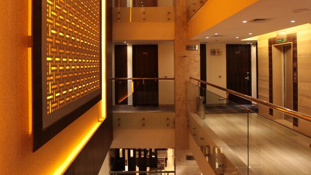Un interior de varios niveles con una escalera central, barandillas de cristal y un revestimiento de pared con diseño.