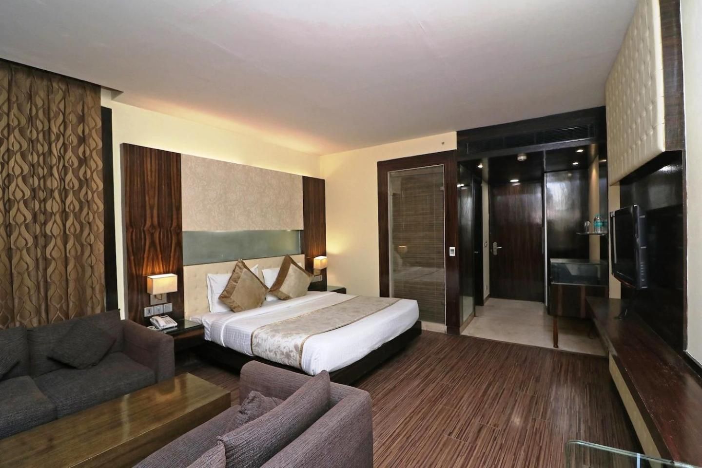 A hotel room with a bed, two bedside tables, a sofa, a television, and a sliding door leading to a bathroom.