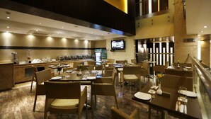 Un comedor de hotel con varias mesas y sillas, una barra de buffet y un televisor montado en la pared.