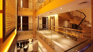 Un interior de varios niveles con una escalera, barandillas de cristal y un revestimiento de pared con diseño.