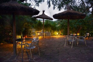 An outdoor patio area with stone flooring, metal chairs, tables, and thatched umbrellas. - Hostal Magnolia (Lloret de Mar)