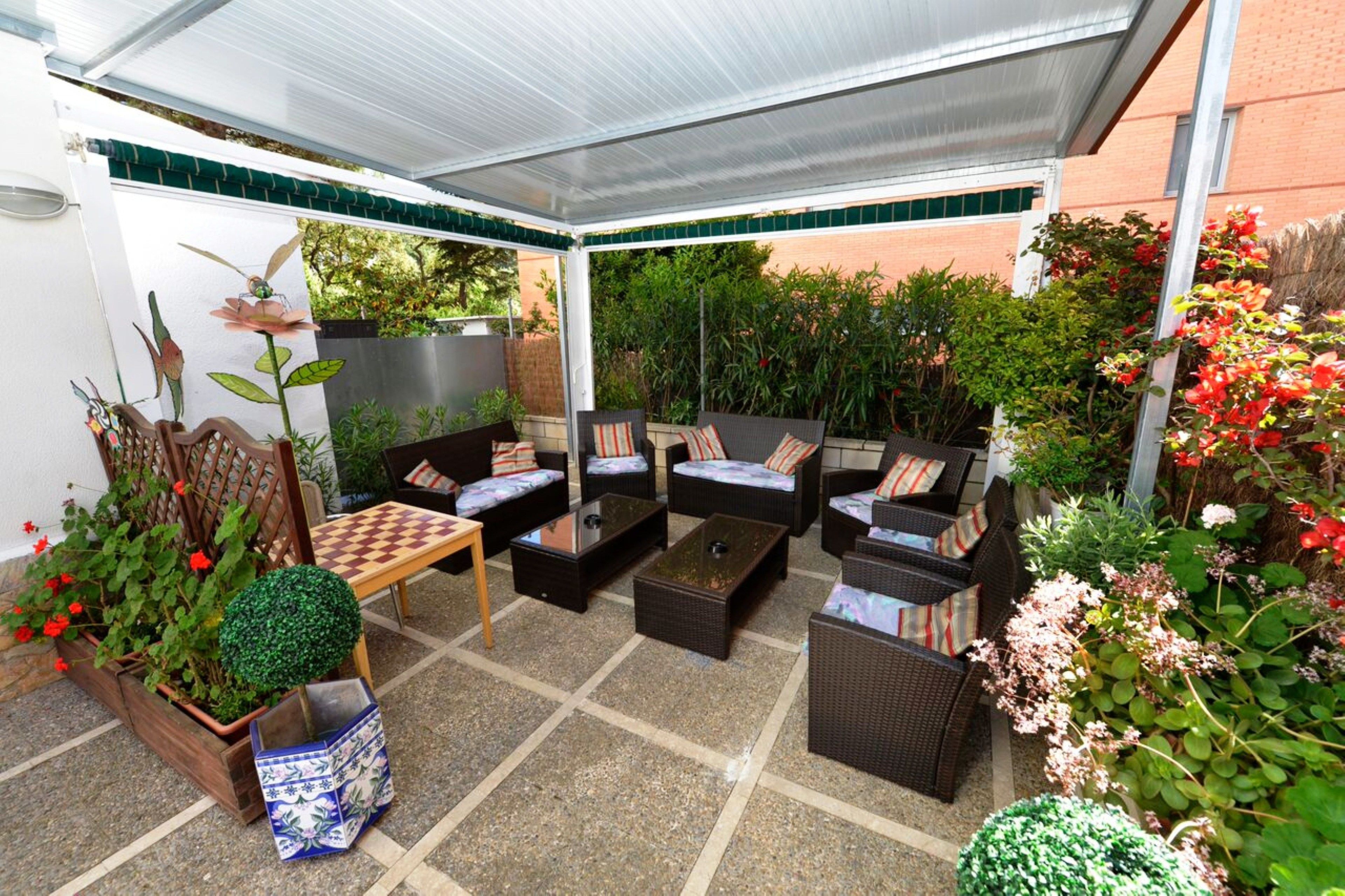 Un área de patio techada con mobiliario de mimbre, una mesa de ajedrez y varios maceteros.