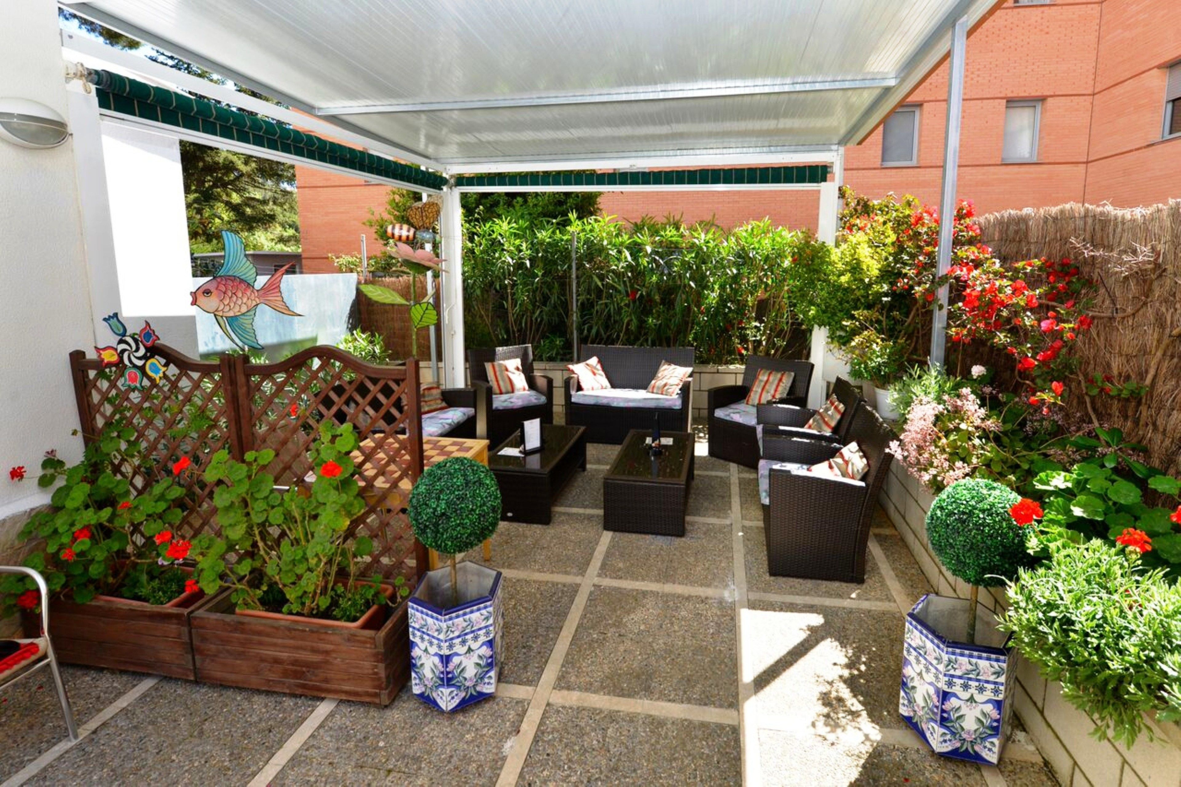 Een overdekte patio met tuinmeubilair, potplanten en een sierhekwerk.