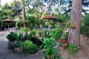 A garden patio with stone planters, a small pond, and thatched umbrellas. - Hostal Magnolia (Lloret de Mar)