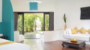 A hotel room with a bed, a sofa, a coffee table, and a view of a tropical garden through a glass door.