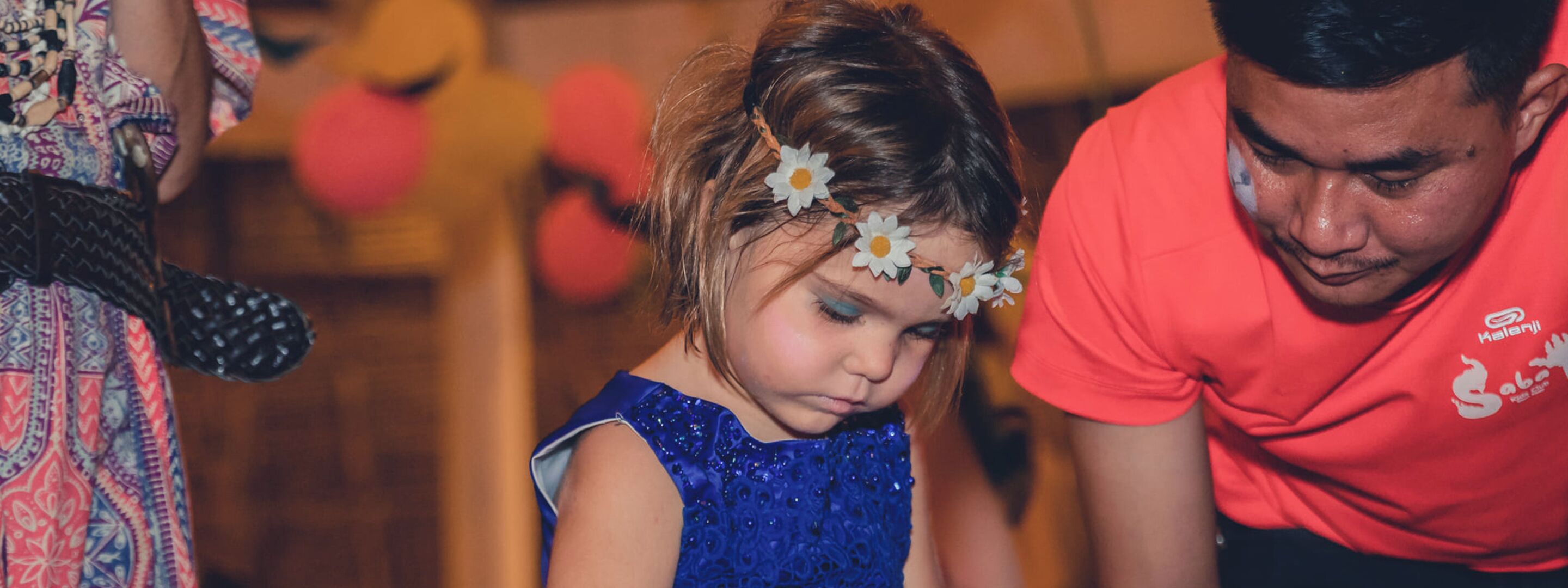 Una persona con camisa roja y un niño con vestido azul y un adorno de flor.