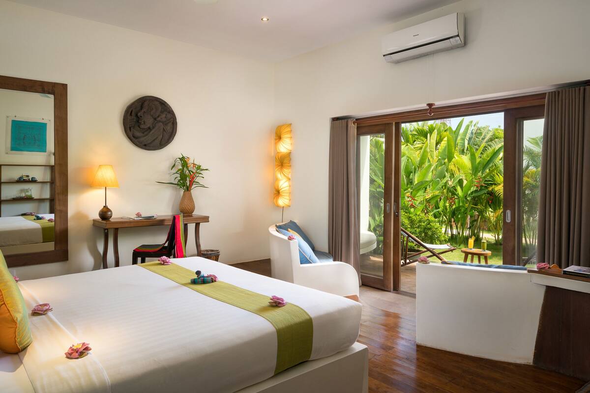A hotel room with a bed, desk, chair, and a view of lush greenery through the sliding glass door.