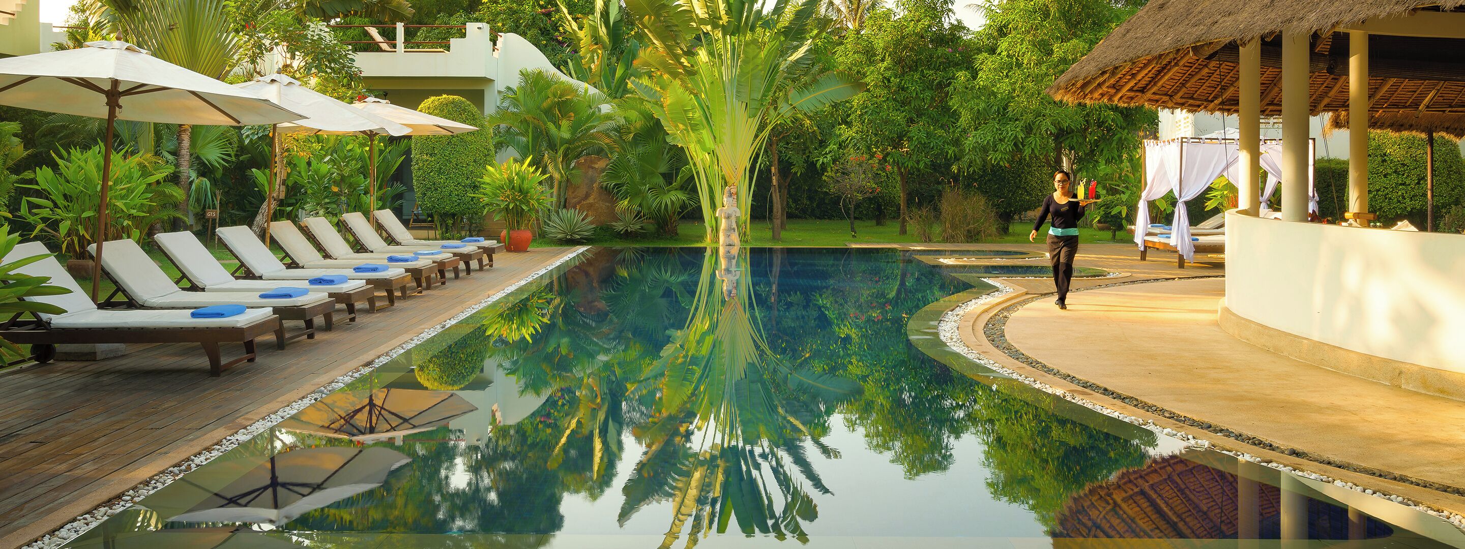Ein Pool mit Liegestühlen und Sonnenschirmen, umgeben von üppiger Vegetation.