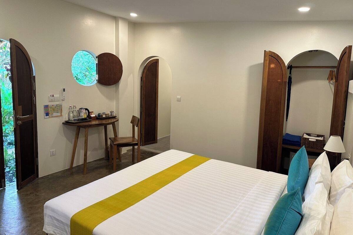 A hotel room with a bed, a desk, and a chair. There are two doors and a mirror.