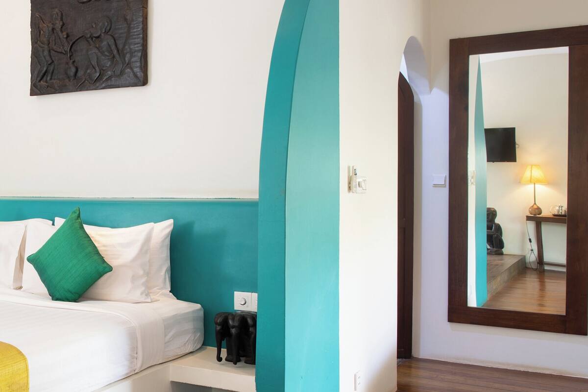 A hotel room with a bed, teal accent walls, a small nightstand, a mirror, and a wall-mounted artwork.