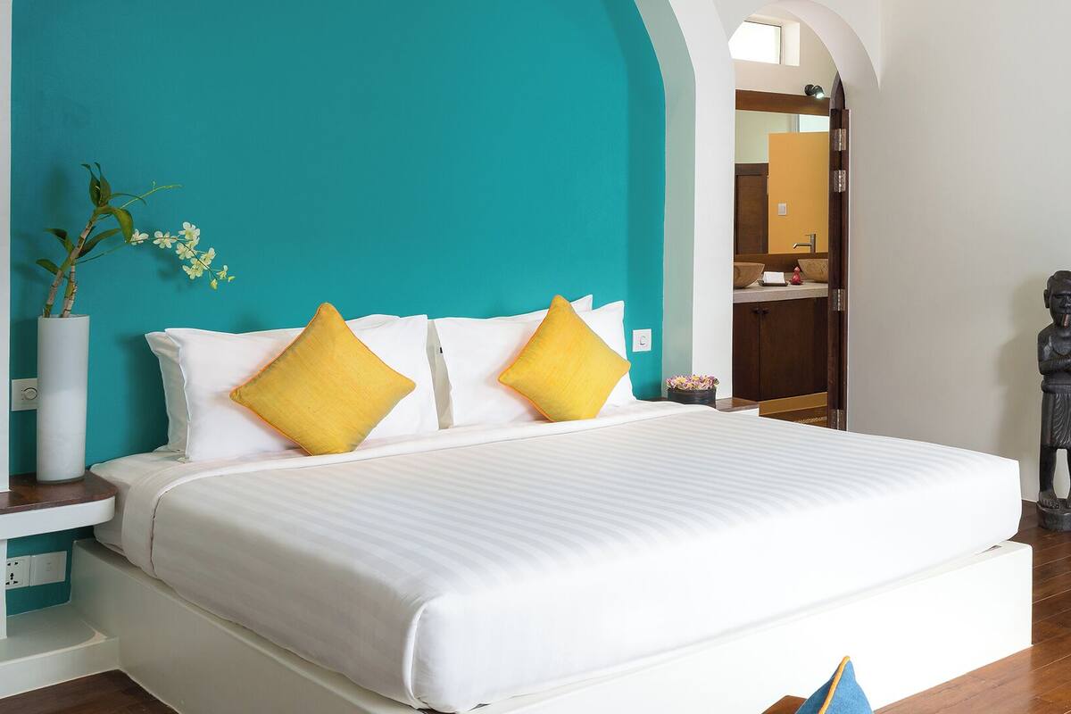 A hotel room with a large bed, a blue sofa, and a mirror reflecting the room.