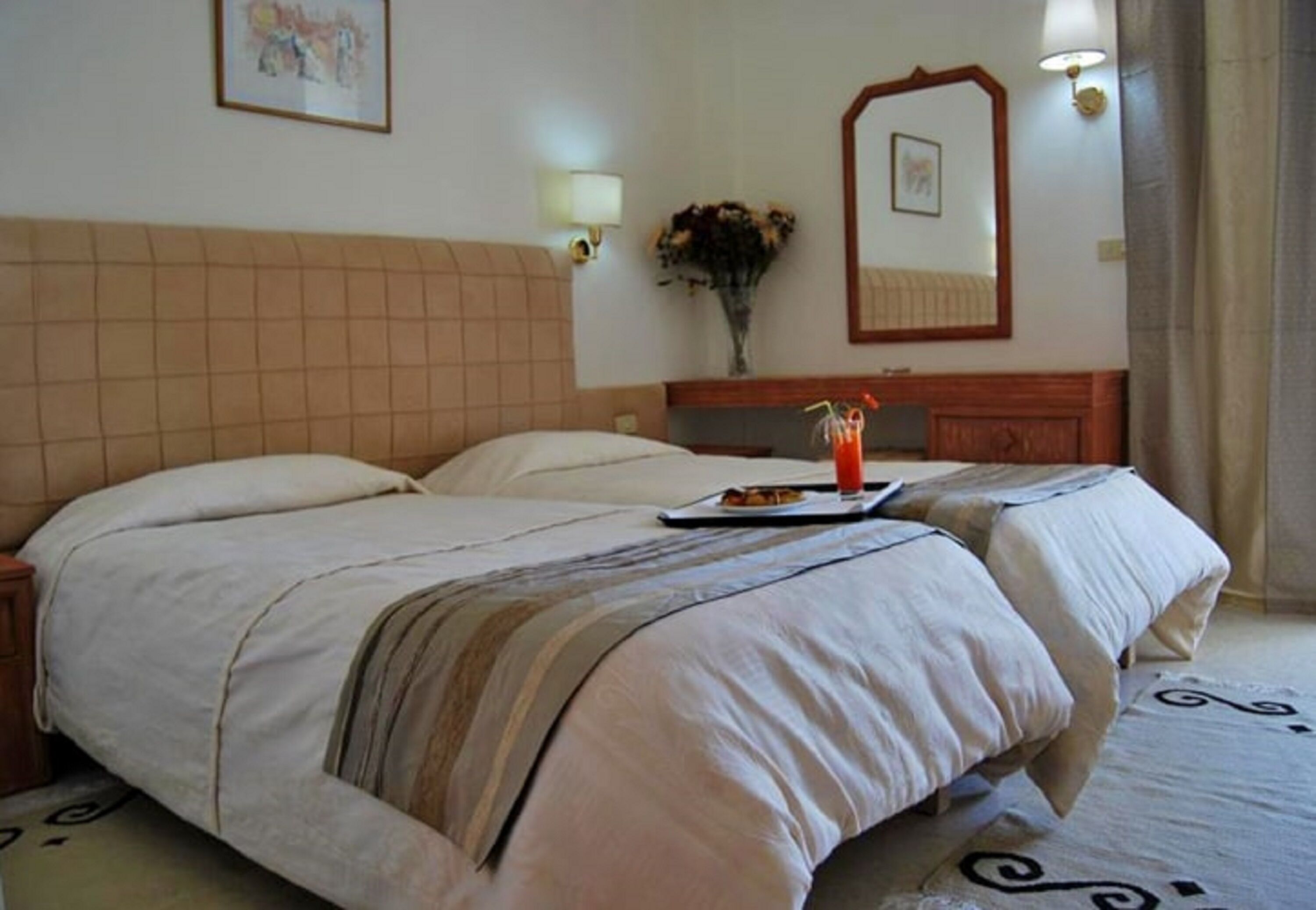 A hotel room with a large bed, a bedside table, a mirror, and a vase with flowers.