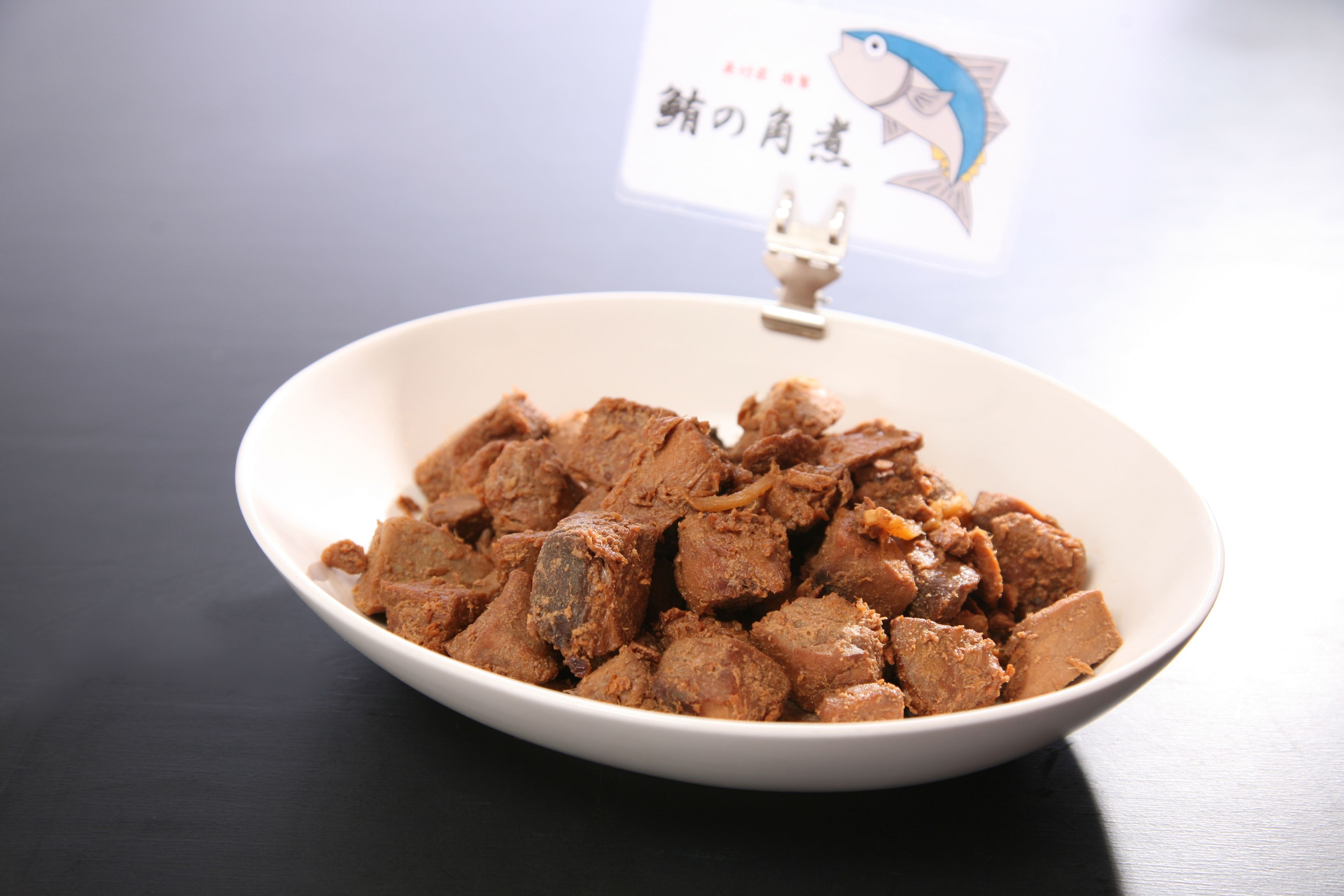 A white bowl filled with a brownish food item, possibly meat, on a dark surface.