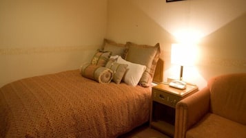 A single bed with a patterned bedspread, a nightstand with a lamp, and a chair.