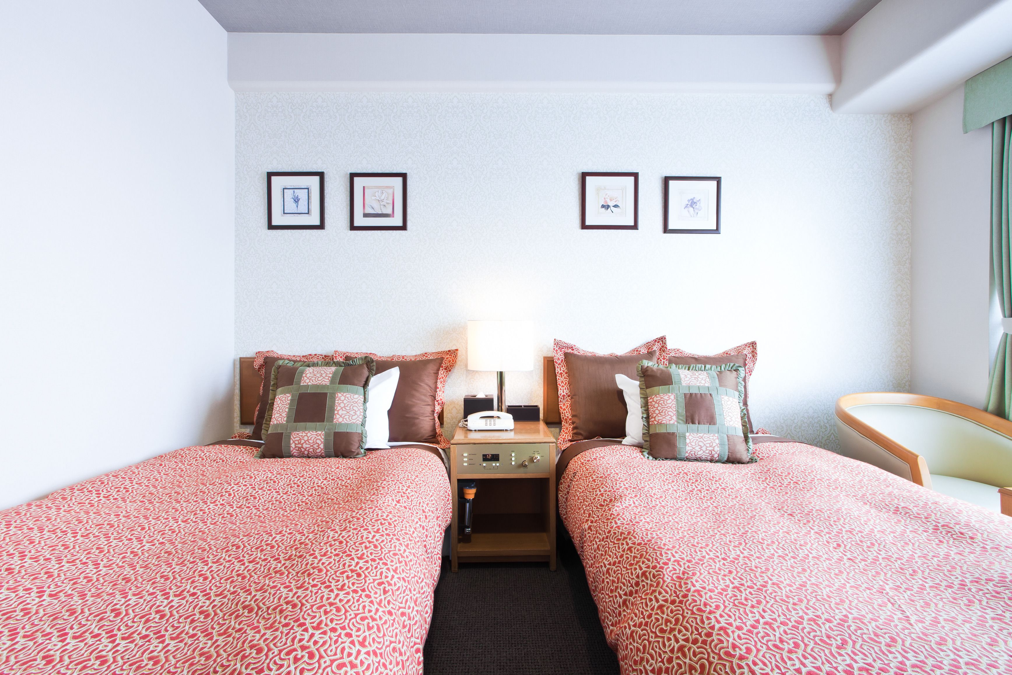 A hotel room with two beds, a nightstand, a lamp, and framed pictures on the wall.