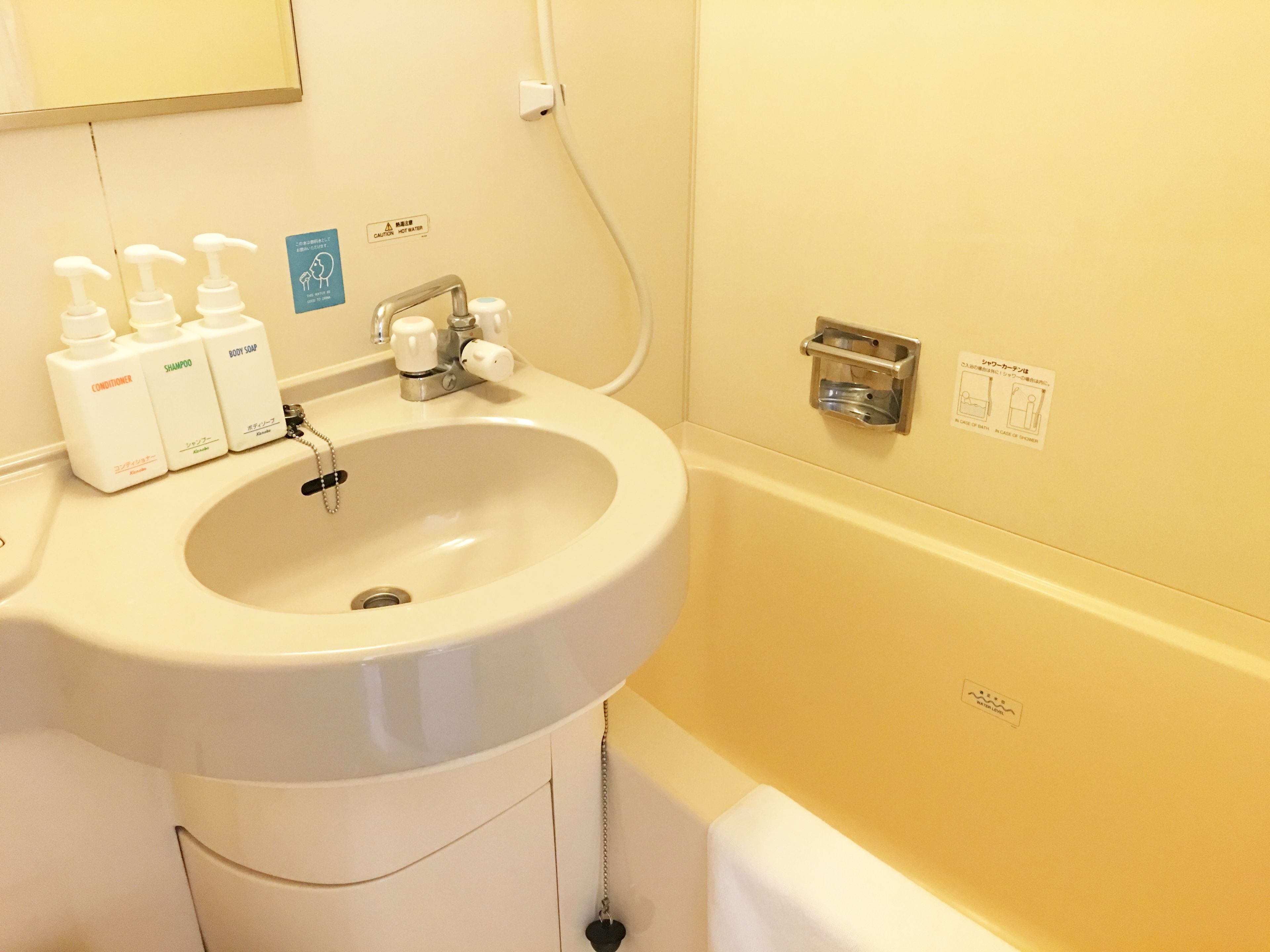 A bathroom with a sink, three bottles of toiletries, a faucet, and a bathtub.