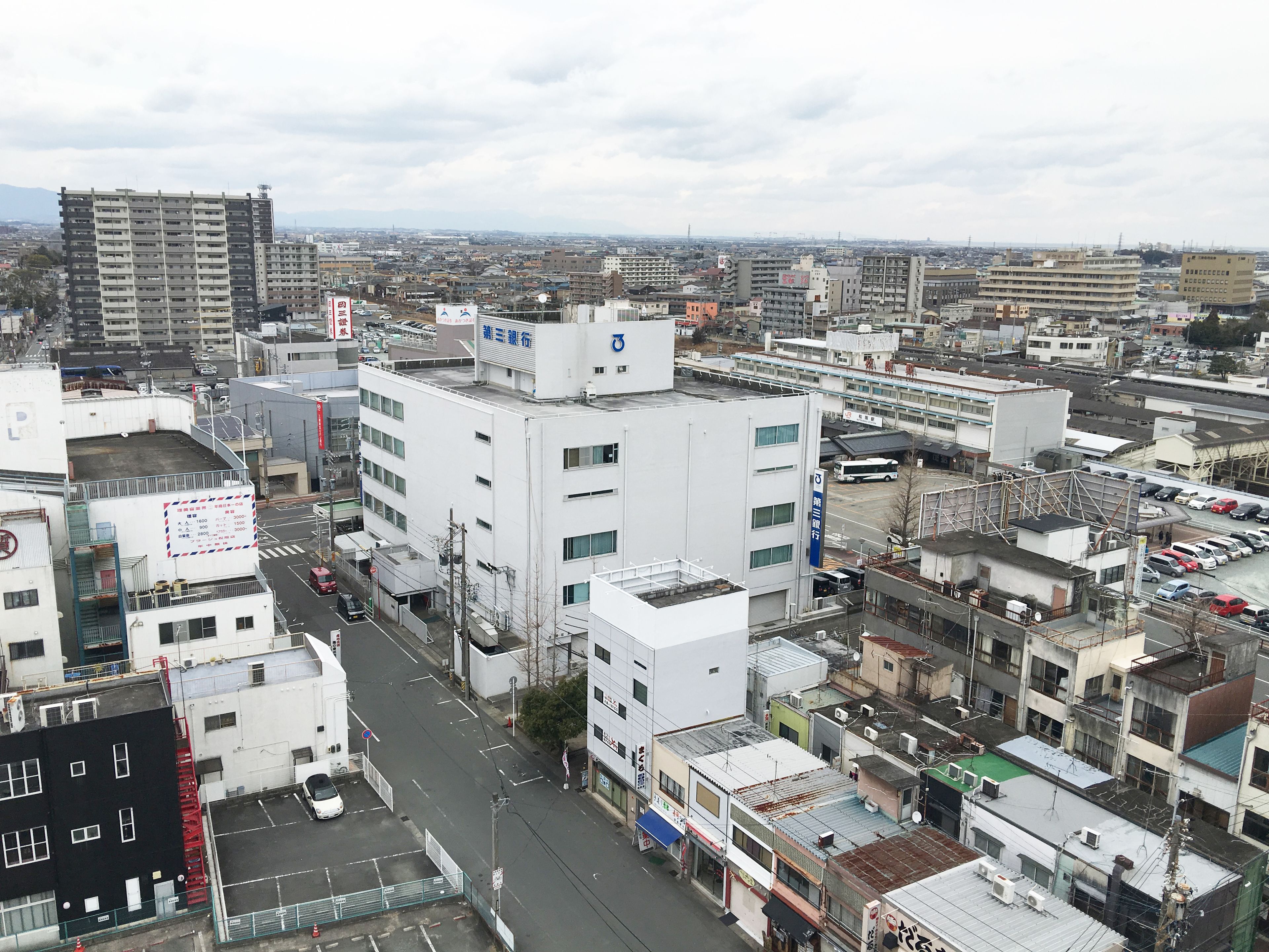 Un paisaje urbano con varios edificios, incluyendo una edificación blanca destacada de varios pisos y un letrero azul en el tejado.