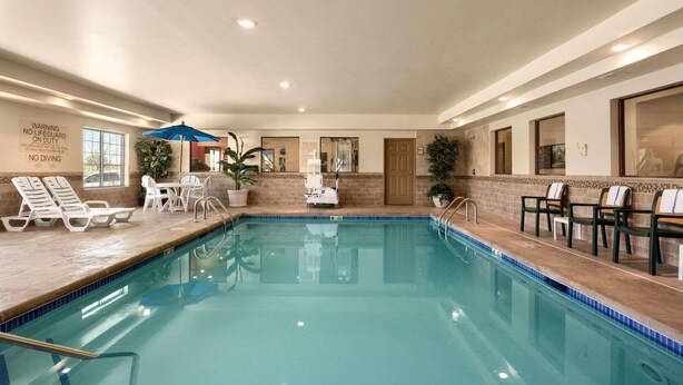 An indoor swimming pool with lounge chairs, a table, and a blue umbrella. - Country Inn & Suites by Radisson, Minot, ND (Minot)