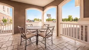 A covered patio with a round table and chairs, a white railing, and a view of a parking lot and buildings. - Country Inn & Suites by Radisson, Minot, ND (Minot)