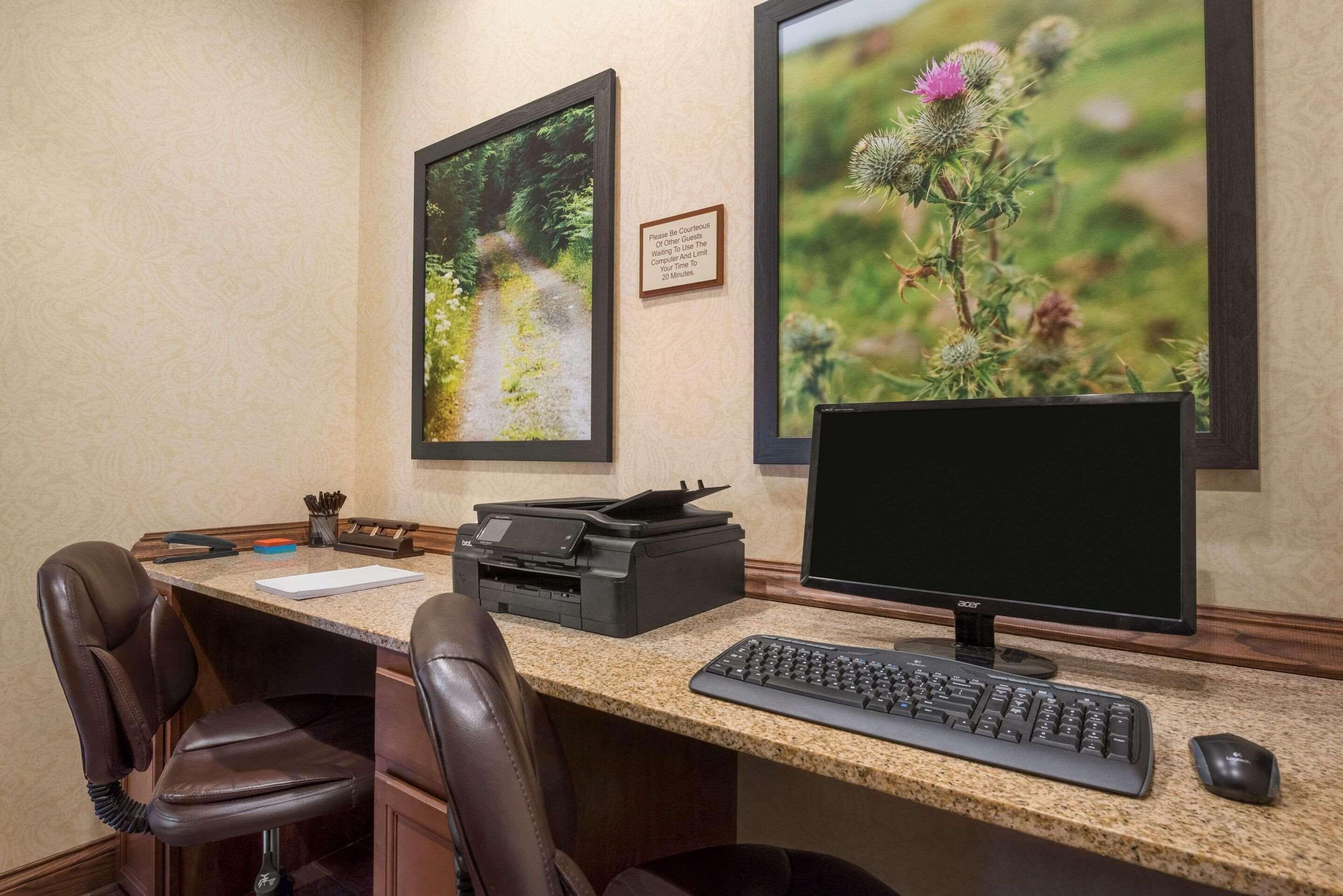 A home office with a desktop computer, two chairs, a printer, and framed pictures on the wall.