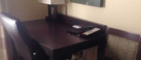 Ein Hotelzimmer mit einem Holztisch, einem Stuhl, einer Lampe, einem Telefon und einem Gemälde einer Berglandschaft.