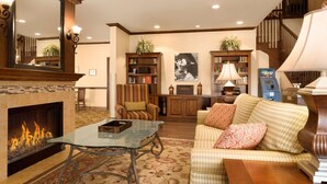 A living room with a fireplace, a sofa, a coffee table, a bookshelf, and a staircase. - Country Inn & Suites by Radisson, Minot, ND (Minot)