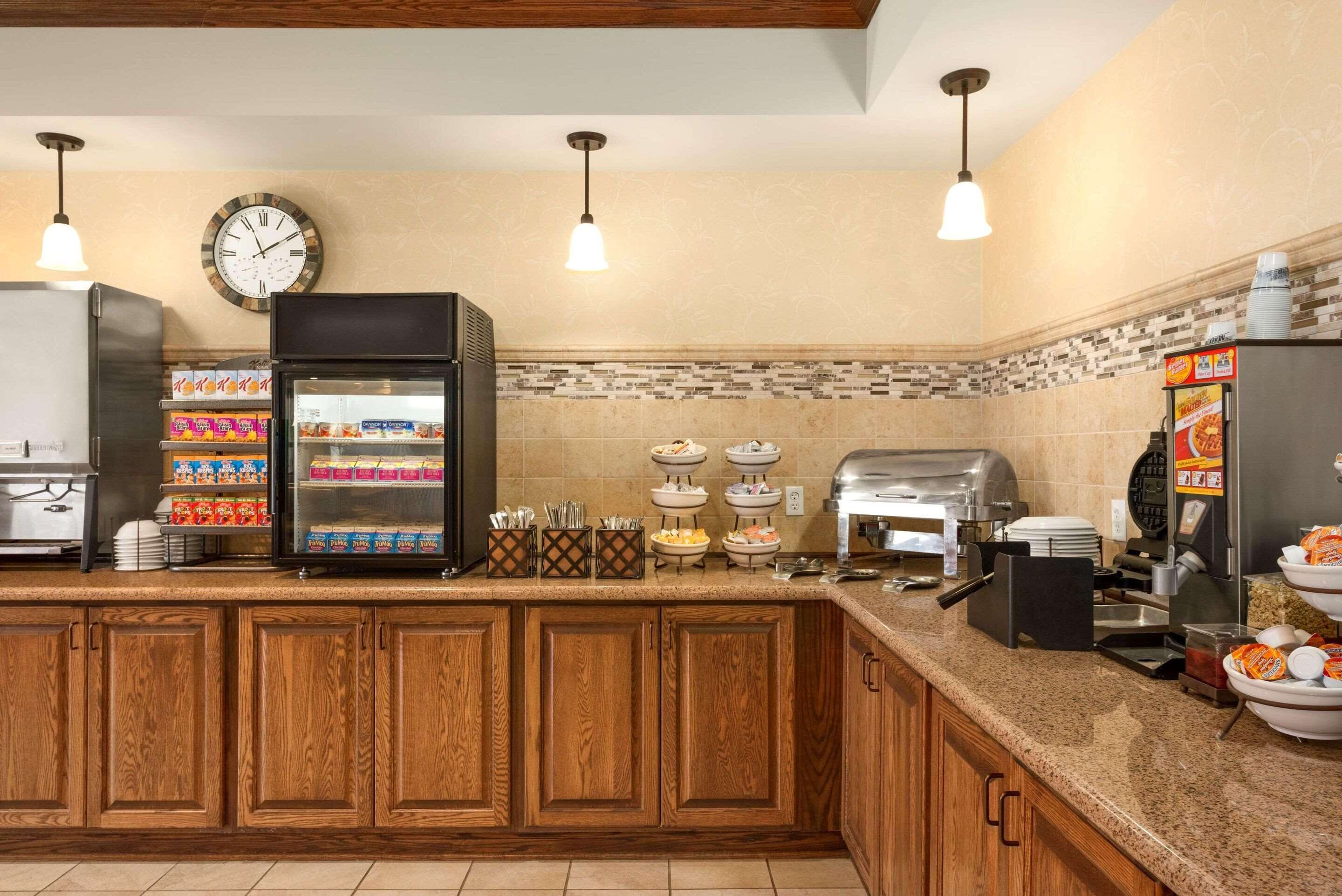 A hotel kitchen with wooden cabinets, a refrigerator, a clock, and various food items on the counter.