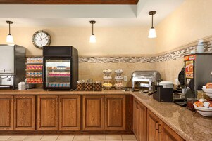 Una cocina de hotel con armarios de madera, un refrigerador, un reloj y diversos alimentos sobre la encimera.