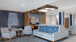 A modern lobby with a grey sofa, armchairs, a small table, and a wall with abstract art. - Holiday Inn Express Hotel & Suites Prattville South by IHG (Prattville)