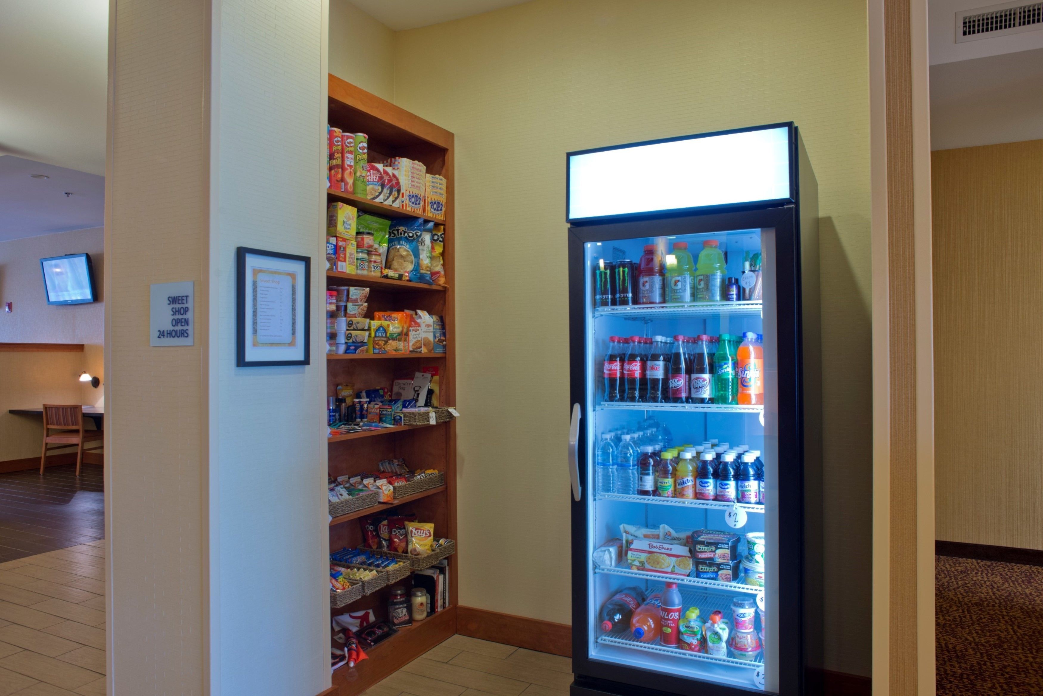 A vending machine stocked with beverages and snacks, a small table with chairs, and a television in the background.