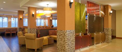 Vestíbulo de hotel con mostrador de recepción, zona de estar y pared decorativa con textura.