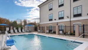 A swimming pool with lounge chairs and umbrellas, surrounded by a building with multiple windows and a brick facade. - Holiday Inn Express Hotel & Suites Prattville South by IHG (Prattville)