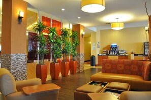Um saguão de hotel com áreas de estar, plantas em vasos e uma mesa de recepção.