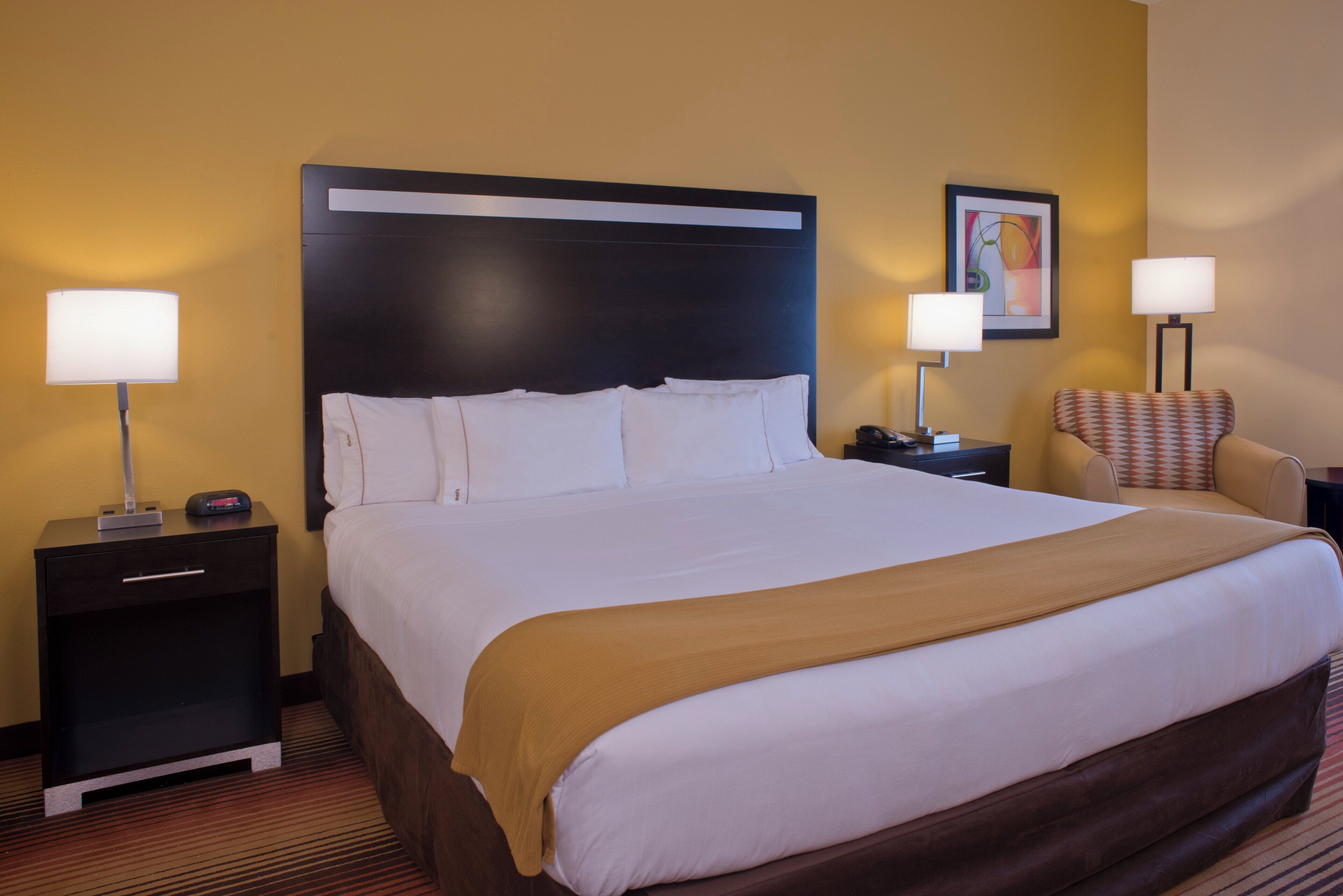 A hotel room with a large bed, two bedside tables, a chair, and a painting on the wall.