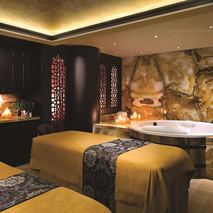 A spa room with two massage beds, a large bathtub, and a marble wall.
