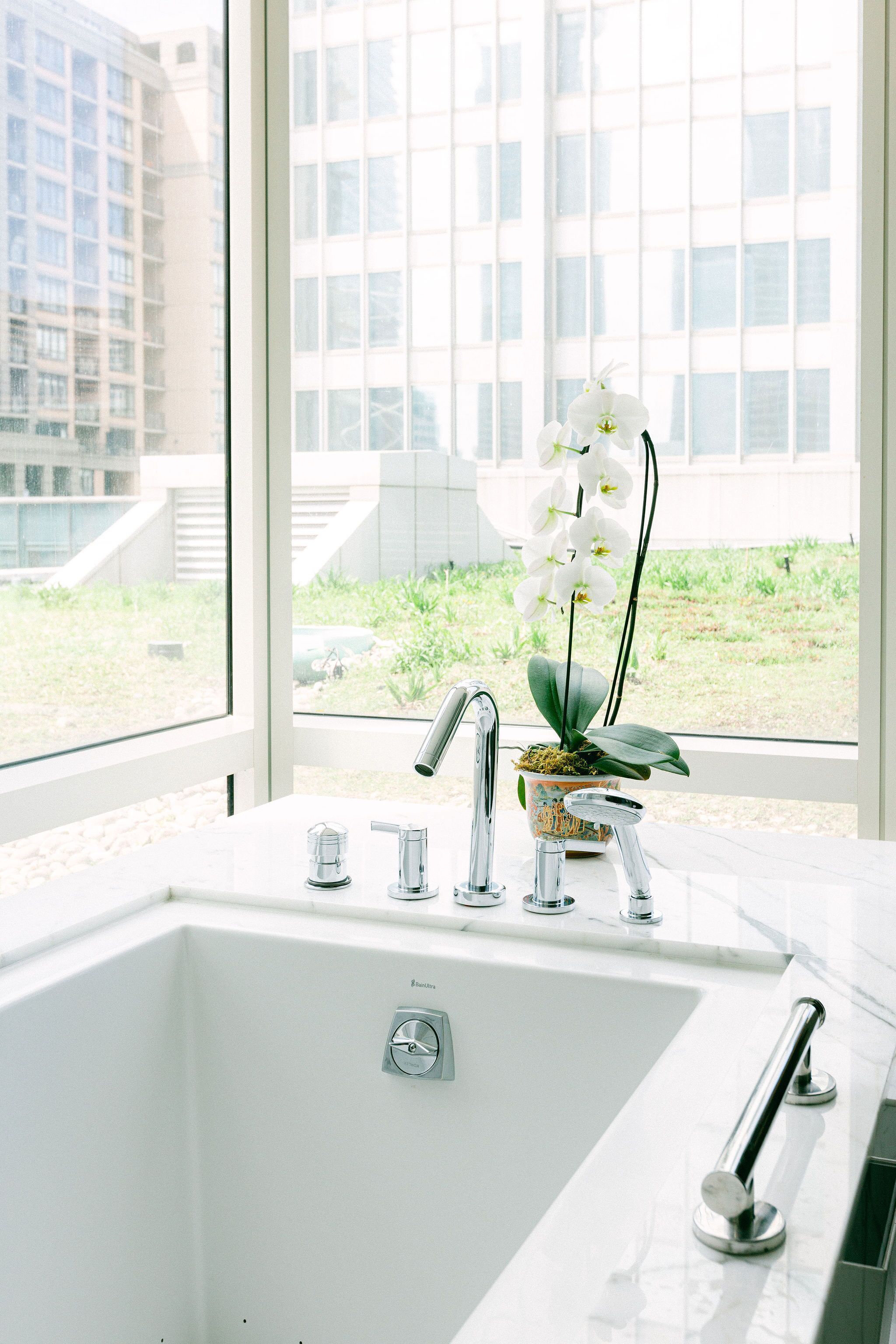 Een moderne badkamer met een witte wastafel, chromen kranen en een potorkidee.