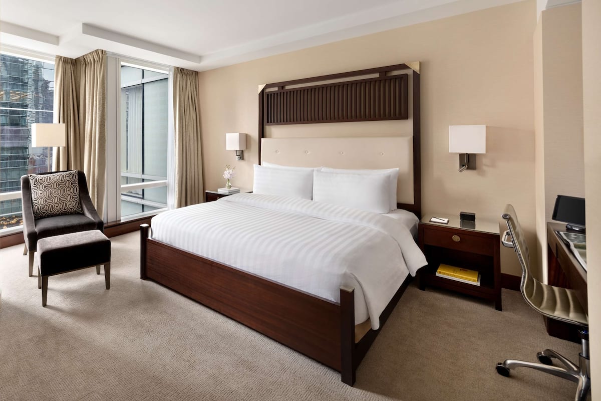 A hotel room with a large bed, a desk, a chair, a nightstand, and a window with curtains.