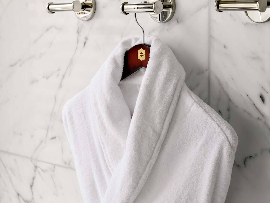 Een witte handdoek hangt aan een metalen handdoekhouder in een badkamer met een marmeren vloer.