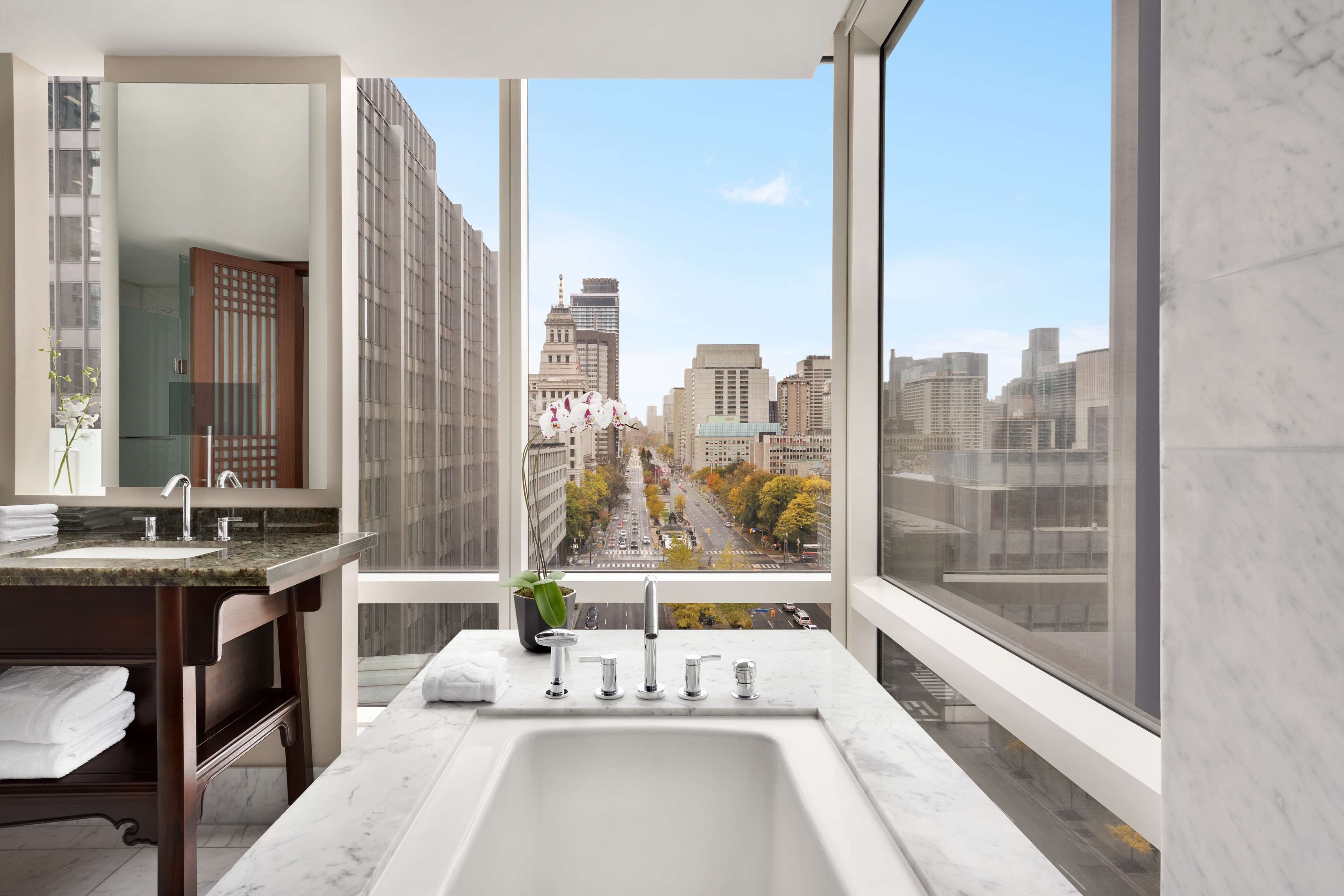 A modern bathroom with a large window, a marble sink, and a view of a cityscape.