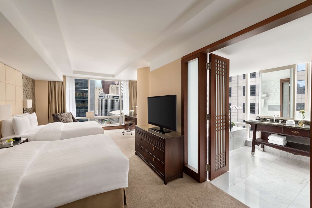 A hotel room with two beds, a TV, a desk, and a bathroom with a large mirror.