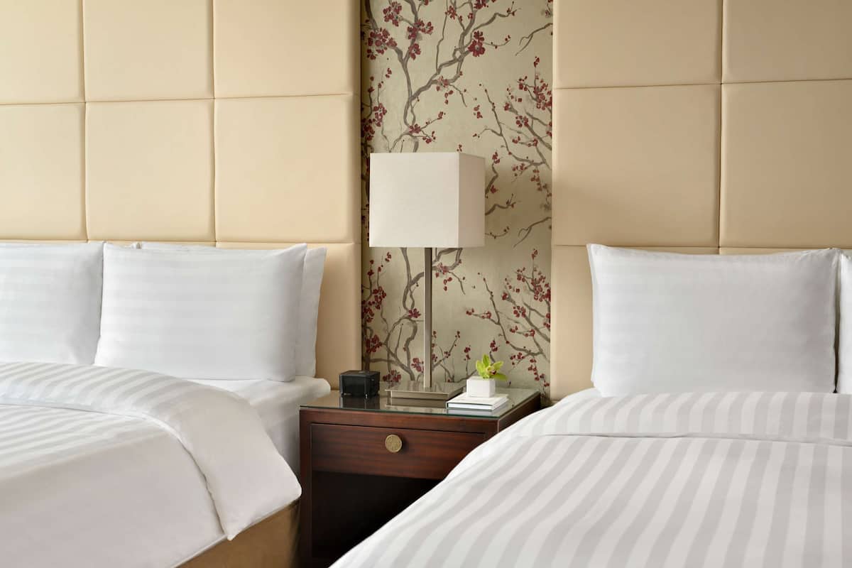 A hotel room with two beds, a nightstand, a lamp, and a floral wallpaper.