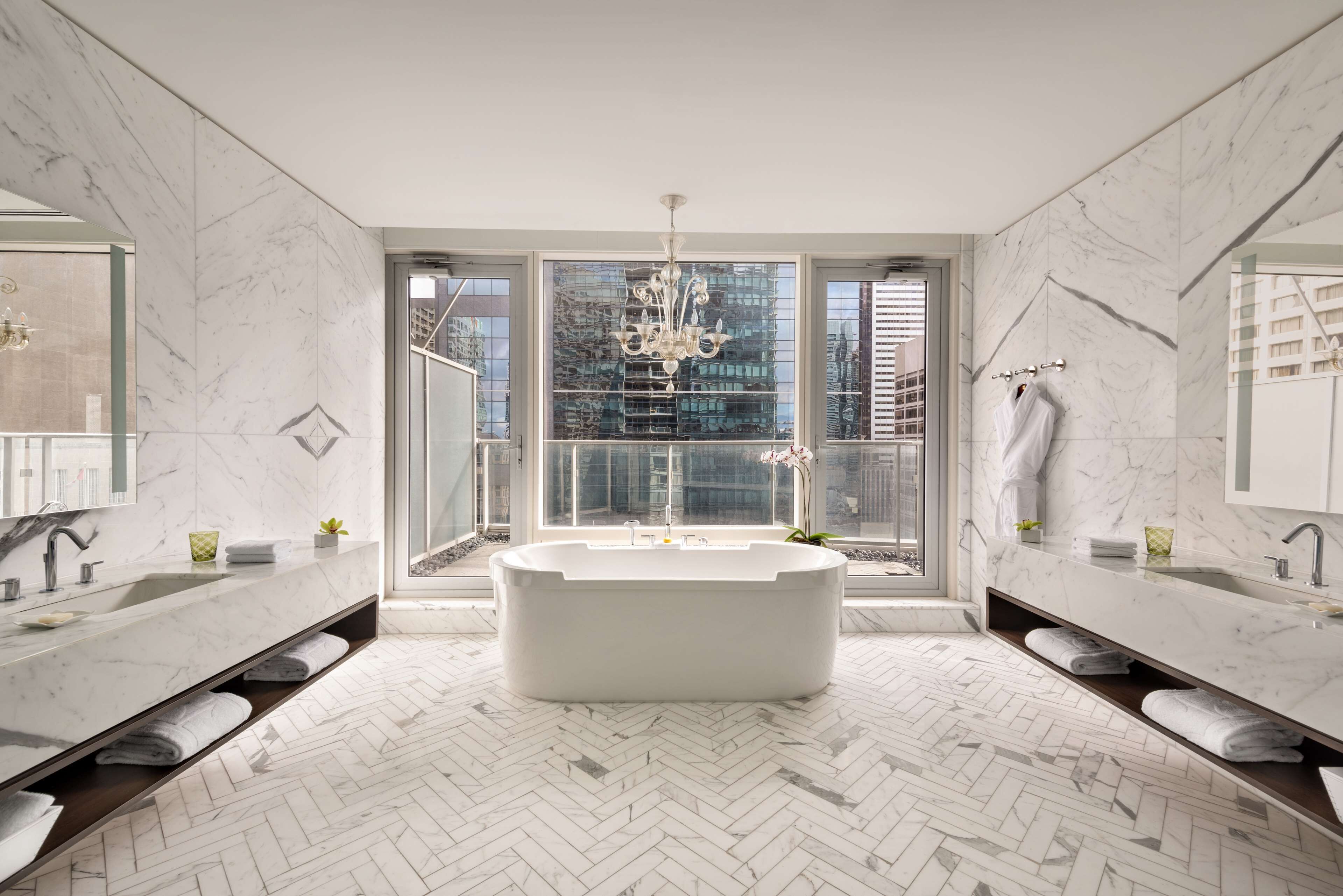 A modern bathroom with a freestanding bathtub, dual sinks, and a large window offering a city view.