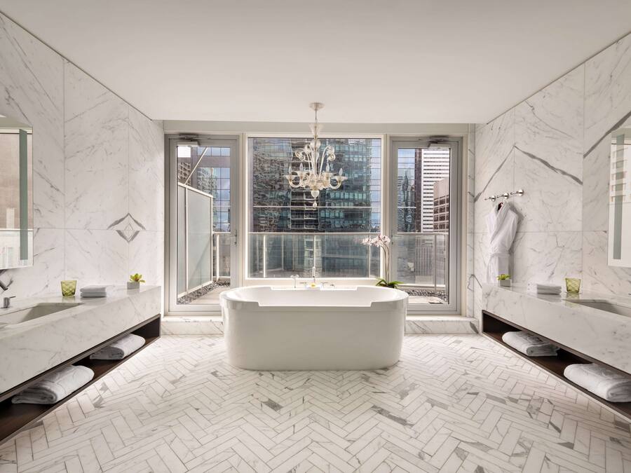 A modern bathroom with a freestanding bathtub, dual sinks, and a large window offering a city view.