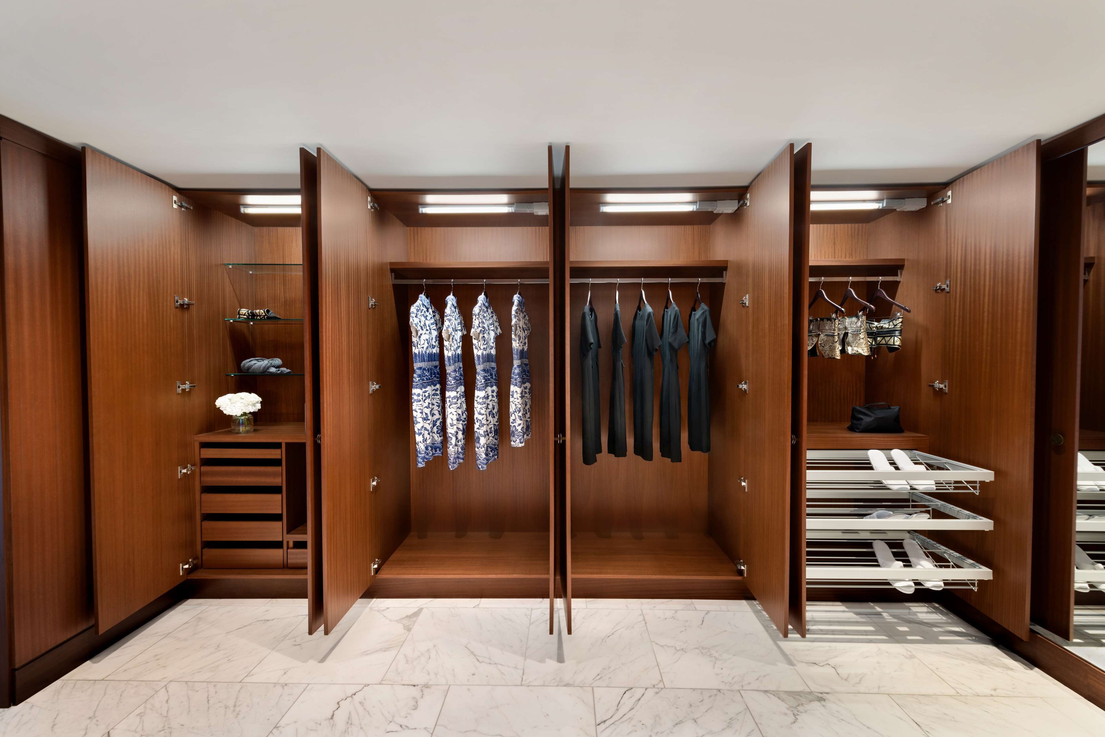 A walk-in closet with wooden doors, a marble floor, and multiple shelves and hanging spaces for clothes and shoes.