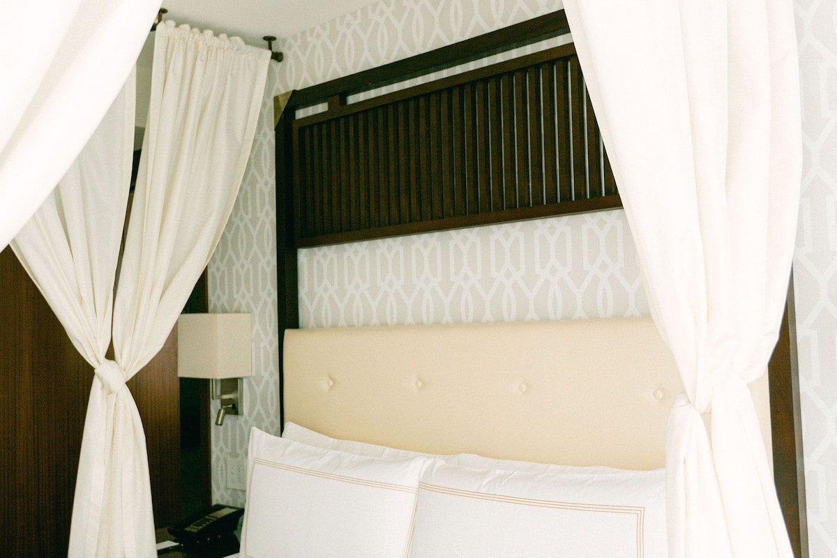 A bed with white linens, a headboard with a patterned design, and a nightstand with a lamp.