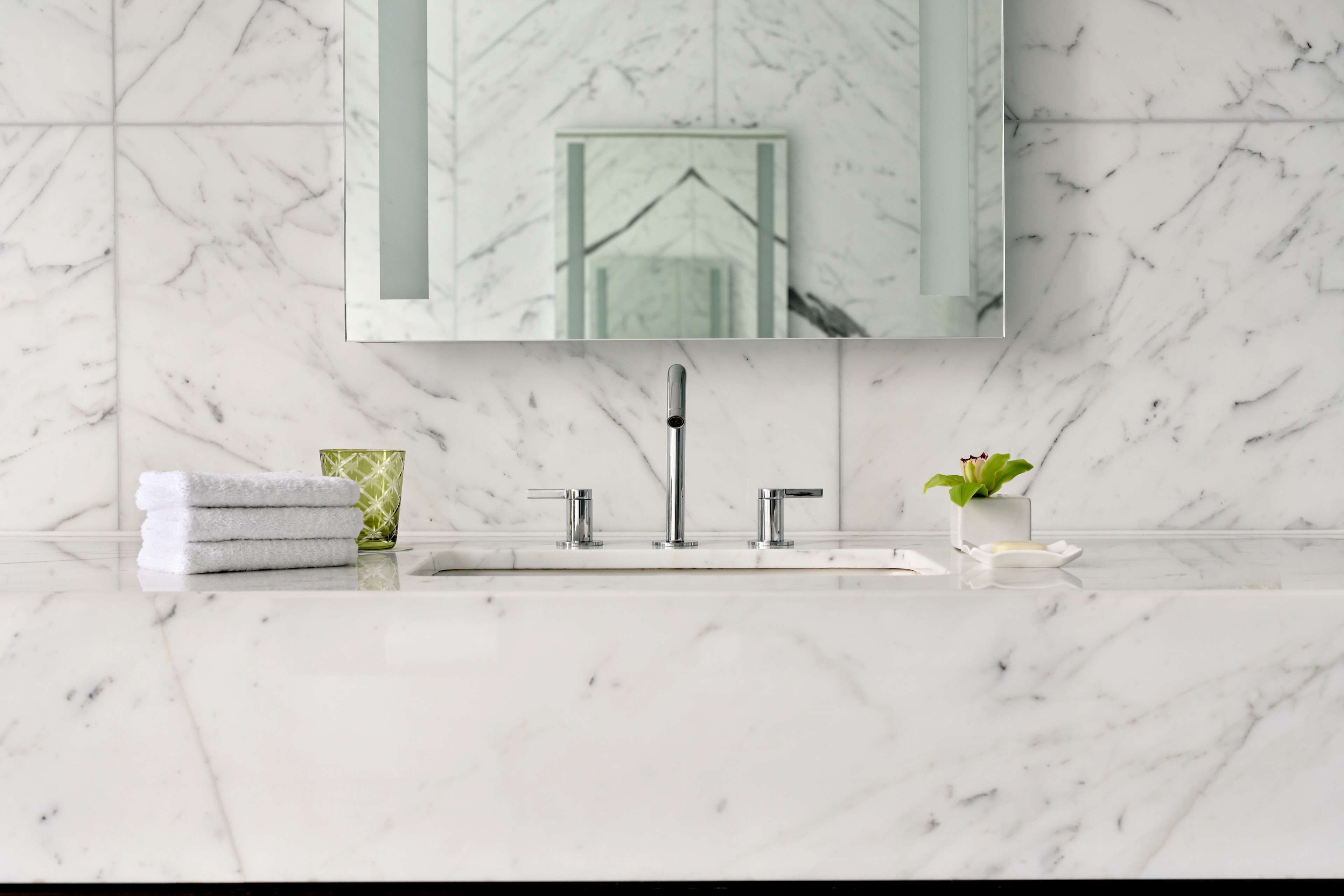 Un bagno con un lavabo in marmo, uno specchio, un asciugamano e una piccola pianta.