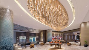 A spacious lobby with a central seating area, a high ceiling with a decorative light fixture, and a large pillar with a mosaic pattern. - The Aarlis Hotel Panchkula, Vignette Collection by IHG (Panchkula)
