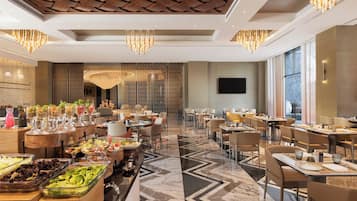 Un amplio comedor de hotel con varias mesas, un bufé con diversas opciones de comida y un moderno candelabro.